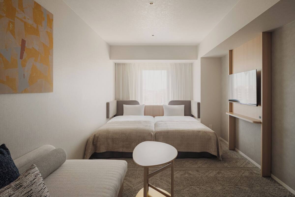 A hotel room with two beds, a small seating area, a flat-screen TV, and a large abstract painting on the wall.
