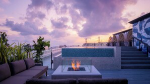 A rooftop terrace with a fire feature, seating, and a view of the cityscape at sunset. - THE NEST NAHA (Naha)