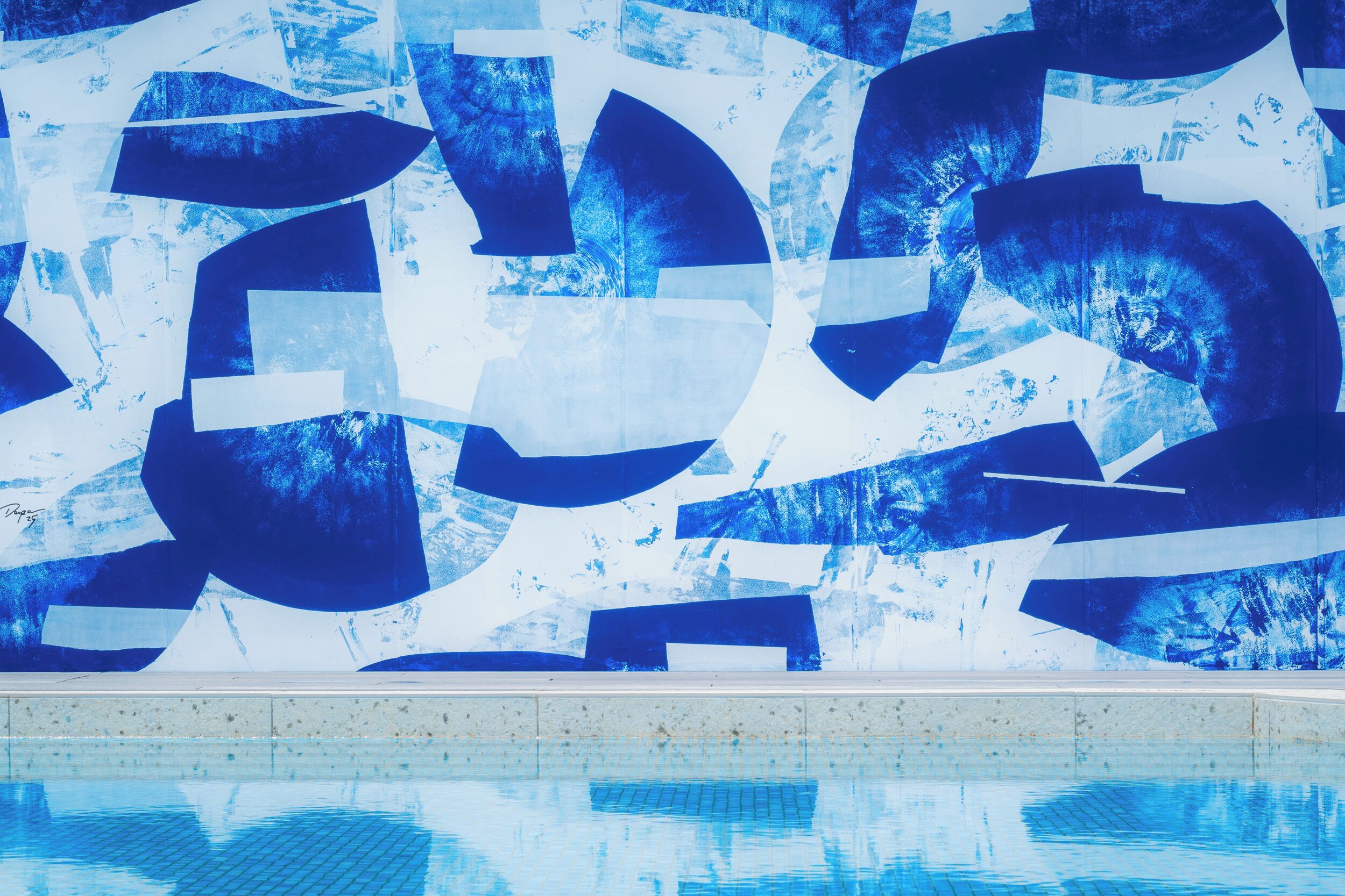Une piscine dont le mur est décoré d’une fresque abstraite bleue.