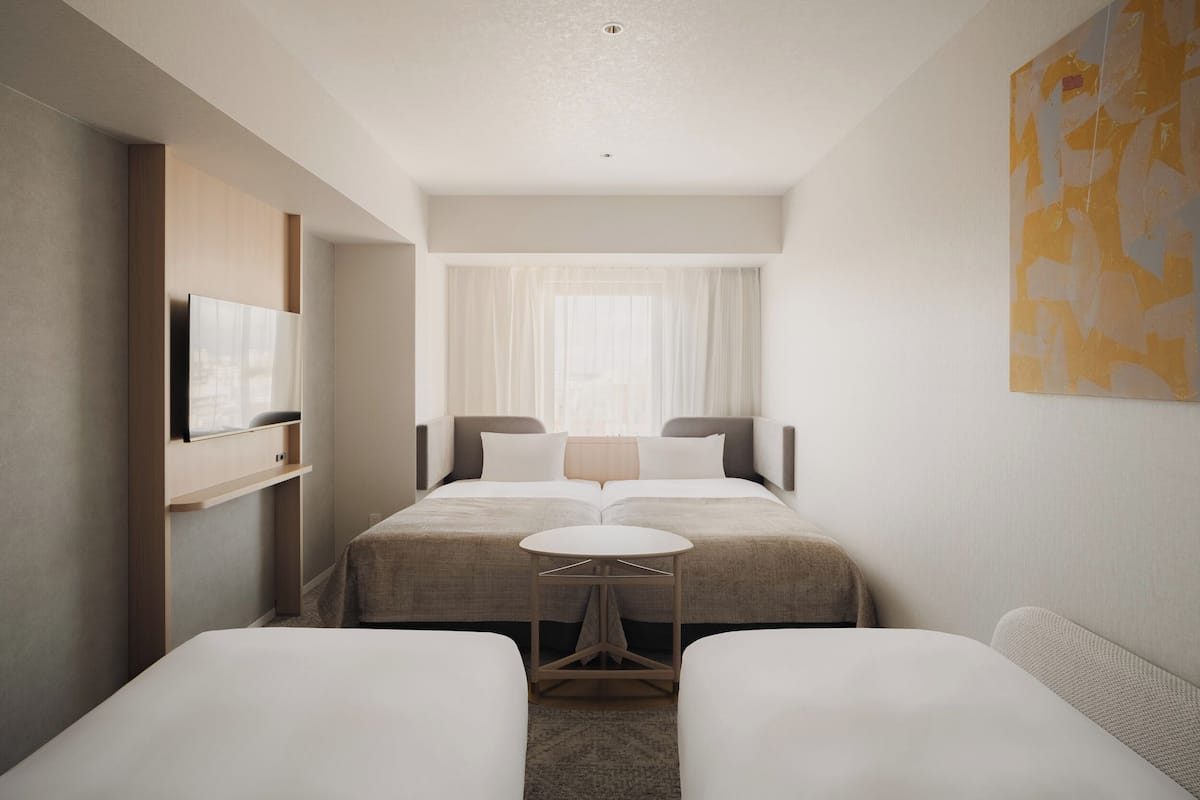 A modern hotel room with a bed, two bedside tables, a TV, and a large window with sheer curtains.