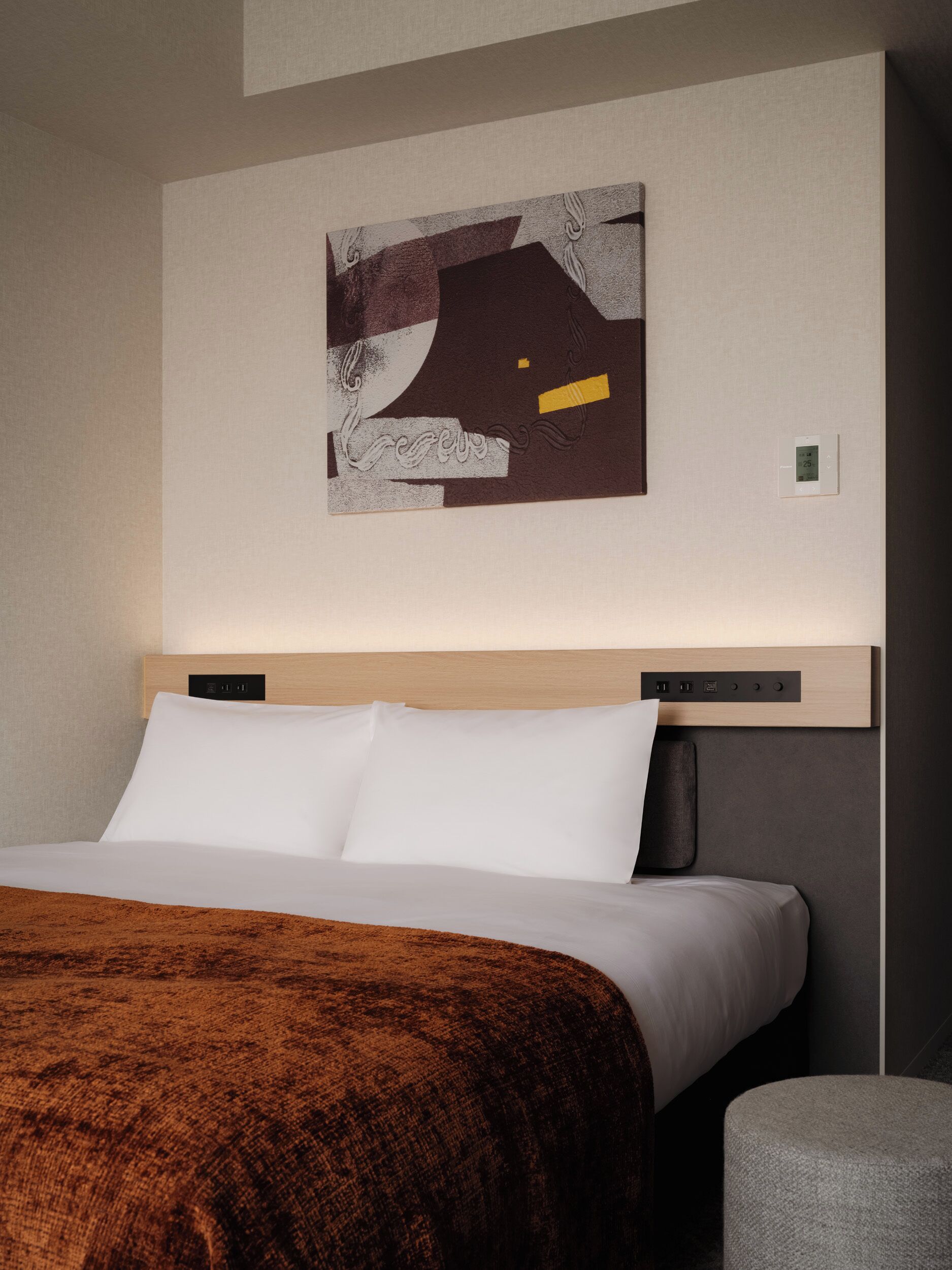 Une chambre d’hôtel moderne dotée d’un grand lit, d’une tête de lit avec des commandes intégrées, d’une œuvre d’art abstraite accrochée au mur et d’une petite table de chevet.