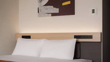 A modern hotel room with a large bed, a headboard with integrated controls, a wall-mounted abstract artwork, and a small bedside table.