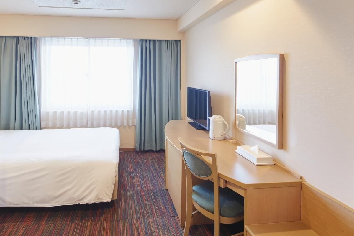 A hotel room with a bed, a desk, a chair, a television, and a window with curtains.