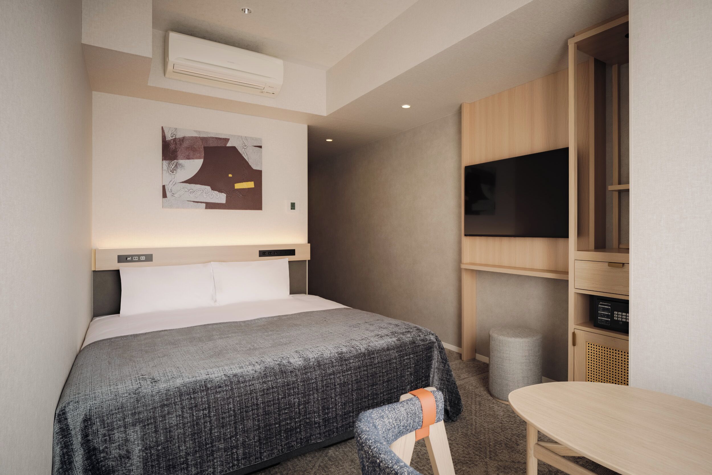A modern hotel room with a bed, a TV, a desk, and a wall-mounted air conditioner.