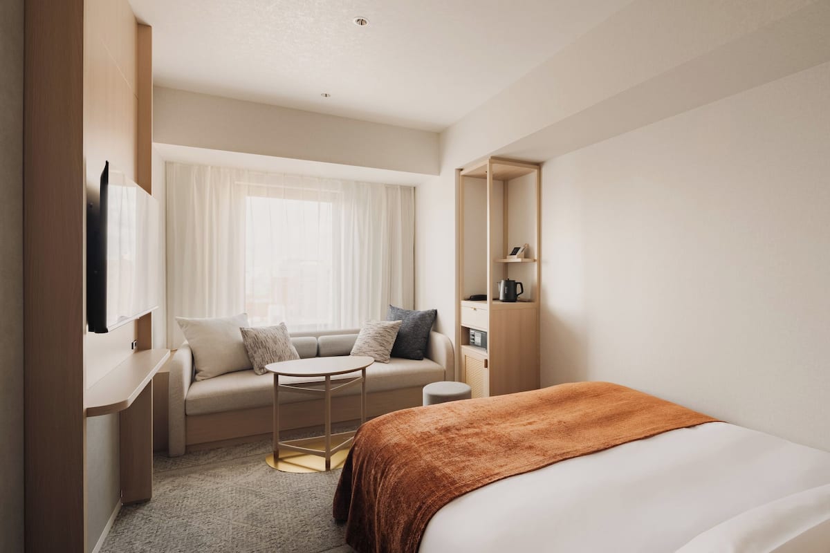 A modern hotel room with a bed, a sofa, a small table, and a TV on a stand.