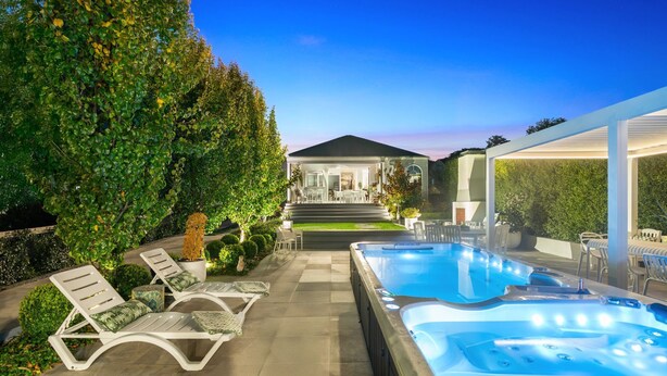 Un espace piscine extérieur moderne, doté de chaises longues, d’un jacuzzi et d’un jardin bien entretenu.