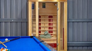 Une table de billard avec des billes, une porte en bois donnant sur une pièce avec des étagères et des murs gris.