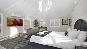 Une chambre spacieuse avec un grand lit, un coin salon comprenant un fauteuil et une petite table, un grand miroir et un tableau représentant des arbres d’automne.