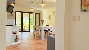 Eine moderne Küche mit Fernseher, ein Essbereich mit Stühlen und eine Glastür, die auf eine Terrasse führt.
