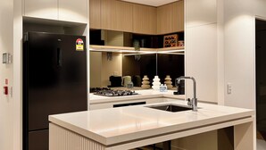 Una cocina moderna con un refrigerador negro, encimeras blancas, un lavamanos de acero inoxidable y armarios de madera.