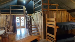 Interior rústico de uma cabana com escada de madeira, beliches e área de jantar.