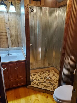 A bathroom with a wooden vanity, a sink, a toilet, and a shower with a corrugated metal door.