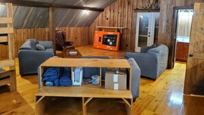 Um quarto de sótão acolhedor com paredes de madeira, um ventilador de teto, um sofá, uma cadeira e um móvel de televisão com um comando remoto.