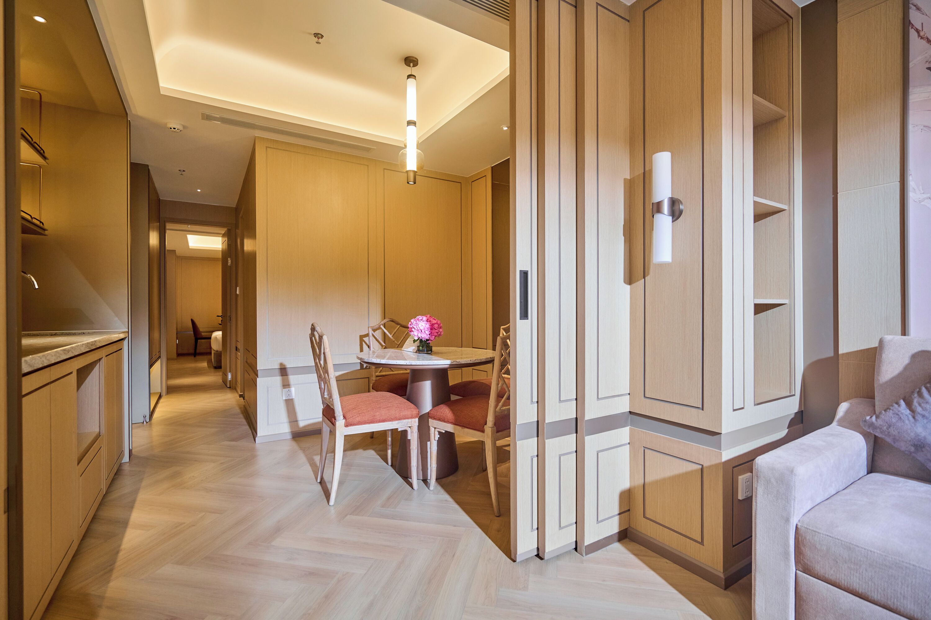 A modern hotel room with a dining area, wooden flooring, and built-in cabinets.