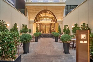 La entrada del Hotel La Passion, con un gran arco, plantas topiarias en macetas y un cartel que muestra el nombre y la dirección del hotel.