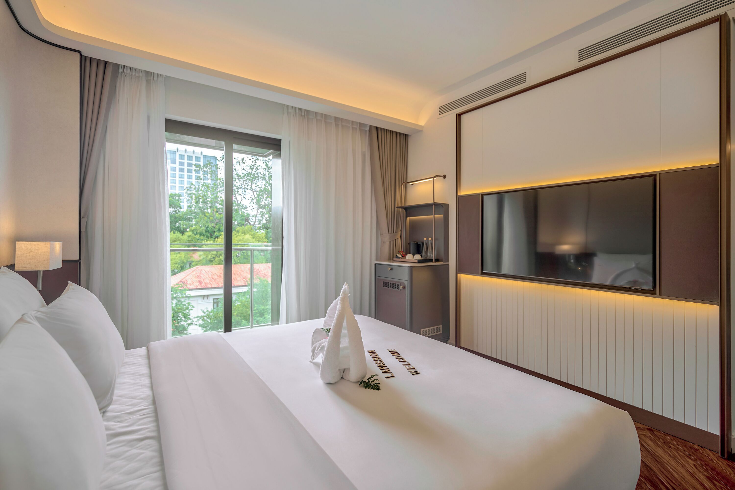Une chambre d’hôtel dotée d’un grand lit, d’un téléviseur à écran plat, d’un minibar et offrant une vue sur la verdure environnante.