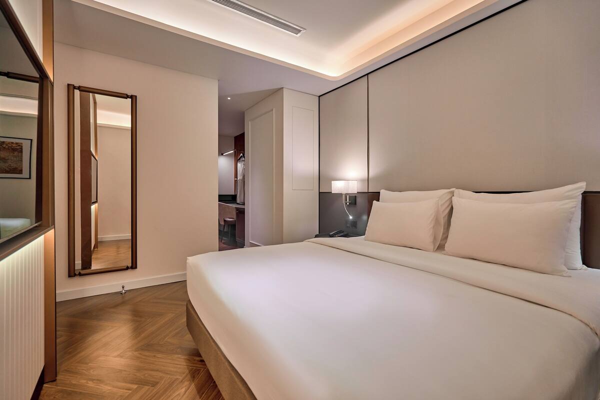A modern hotel room with a large bed, a bedside table, a mirror, and a wardrobe.
