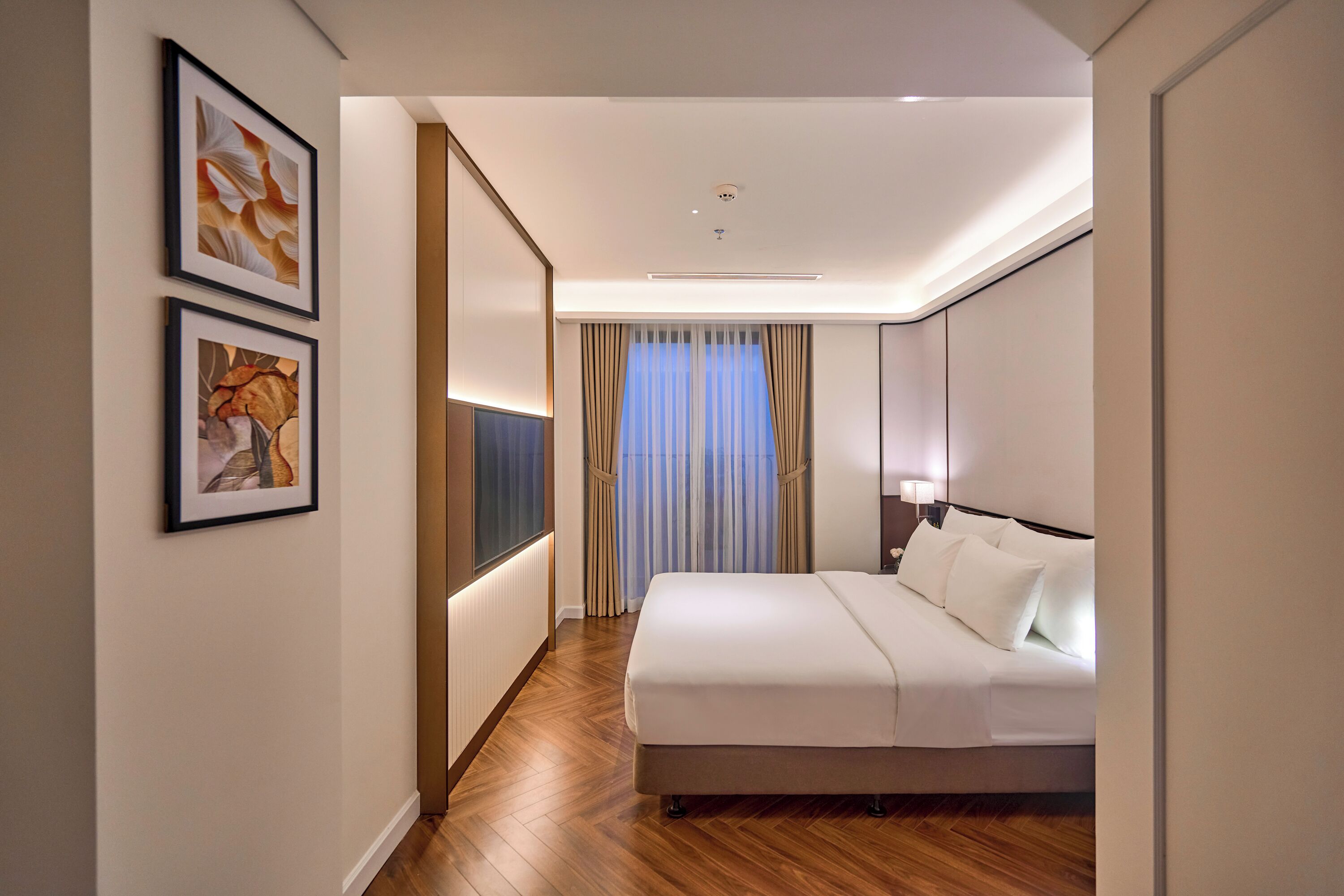 A hotel room with a bed, a TV, and framed artwork on the wall.