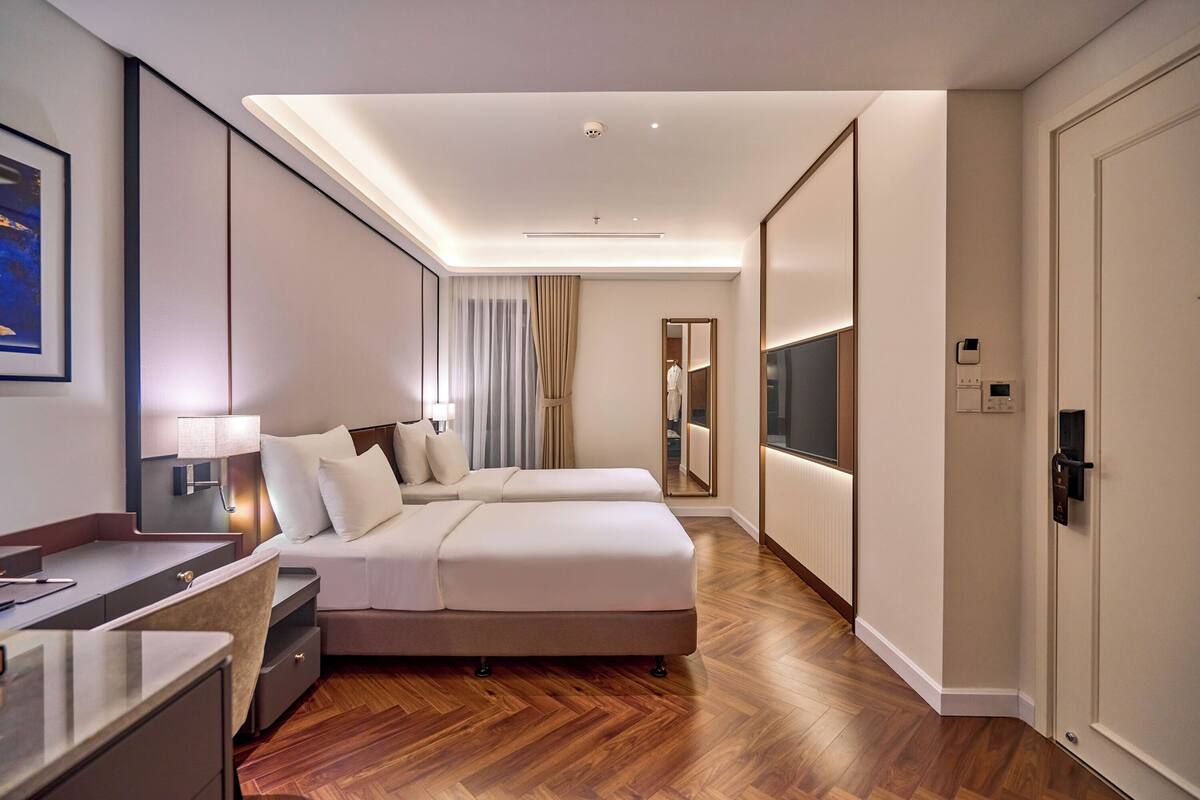 A modern hotel room with a large bed, bedside tables, a desk, and a TV.