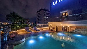 A rooftop pool area with lounge chairs, a water feature, and a building with 'LA PASSION' illuminated signage.