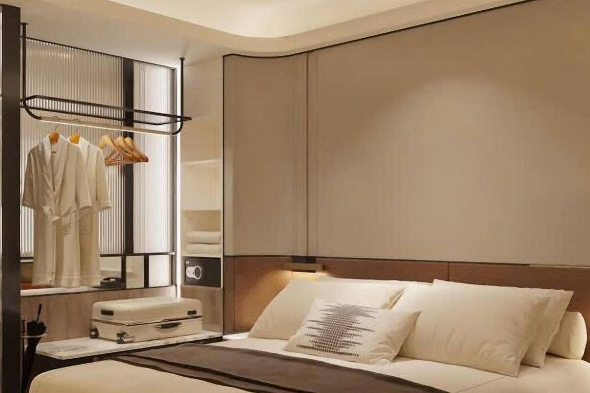A modern hotel room with a large bed, a bedside table with a lamp, a wardrobe, and a mirror.