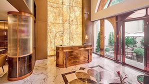 A modern lobby with a marble floor, a reception desk, and large windows offering a view of the outdoor area.
