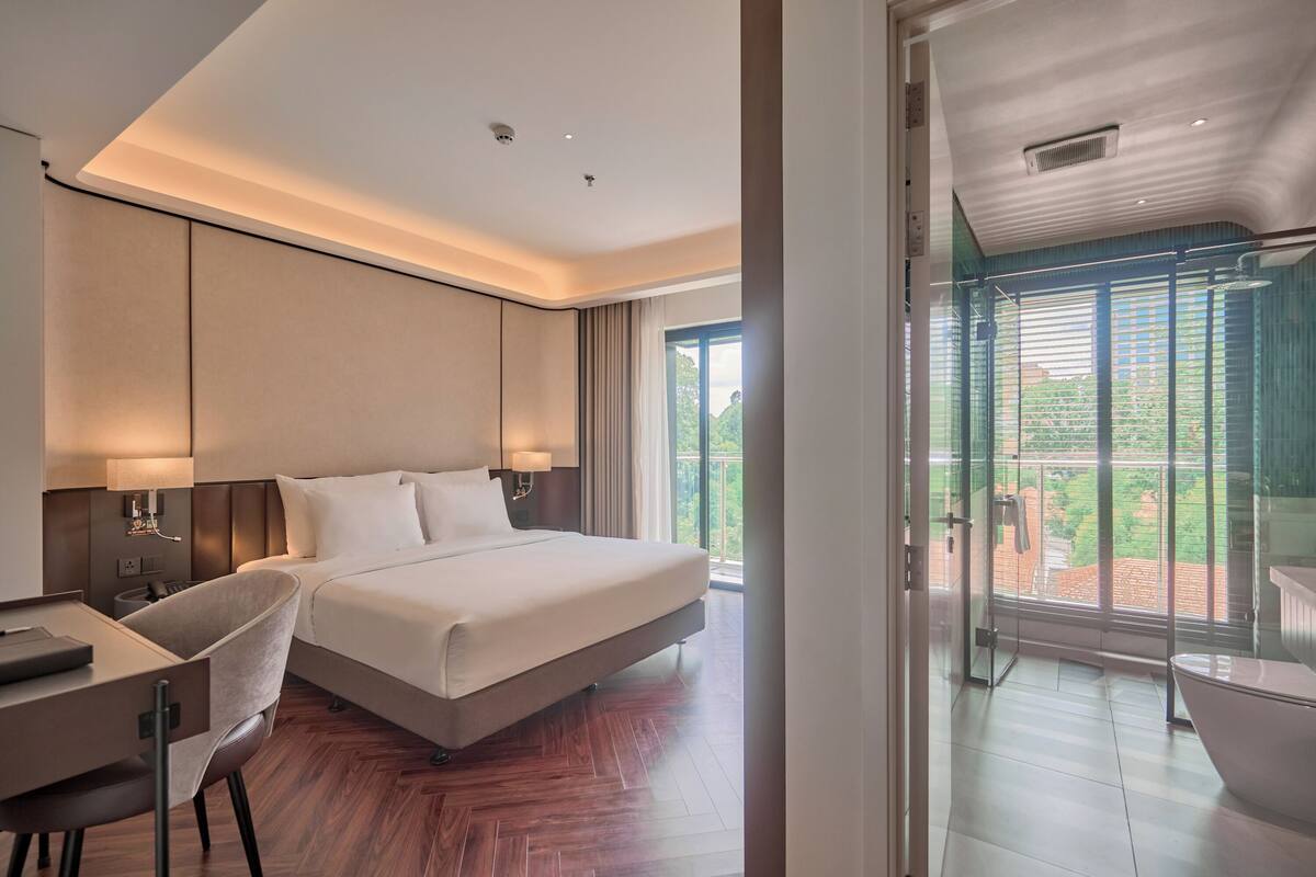A modern hotel room with a large bed, a desk, and a glass-enclosed balcony.