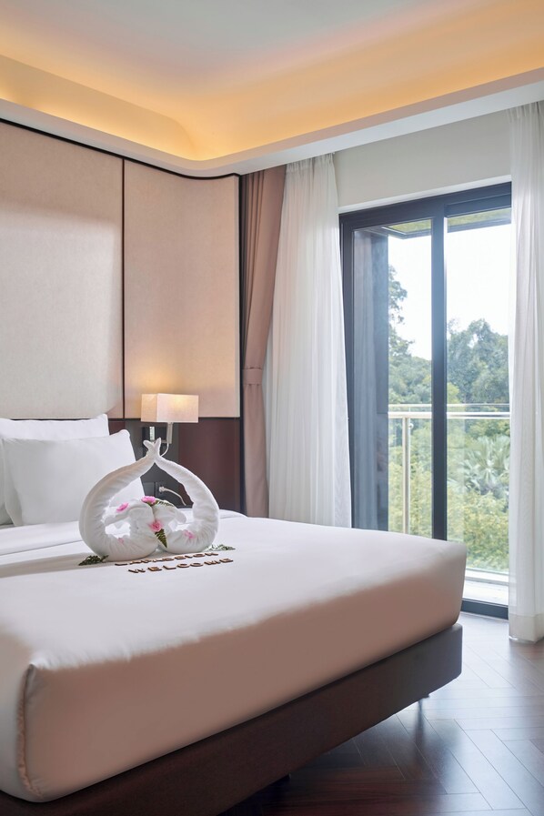 Habitación de hotel con una cama grande, una mesita de noche con lámpara, un cisne decorativo sobre la cama y vistas a zonas verdes por la ventana.