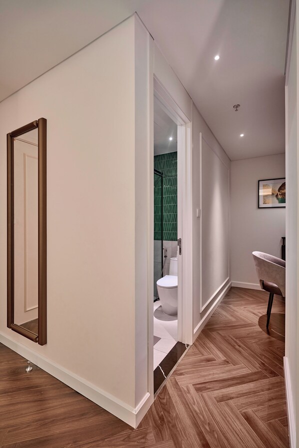 A hallway with a wooden floor, a large mirror, and a door leading to a bathroom with a green shower area.
