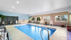 An indoor swimming pool with lounge chairs and tables, surrounded by large windows and a light blue wall. - Red Lion Inn & Suites Blue Springs (Blue Springs)