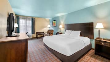 Habitación de hotel con una cama grande, dos mesitas de noche con lámparas, un escritorio con ordenador, una silla y una ventana con cortinas.