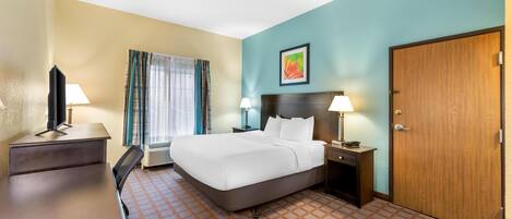 A hotel room with a bed, bedside tables, a desk, a television, and a window with curtains.