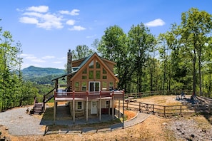 Uma cabana com varanda, rodeada por árvores e vista para a montanha.