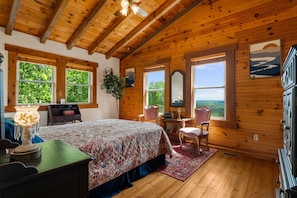 Quarto de cabana de madeira com cama, duas cadeiras, escrivaninha e cômoda.