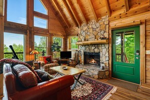 A log cabin interior with a stone fireplace, a green door, a leather couch, and a television.