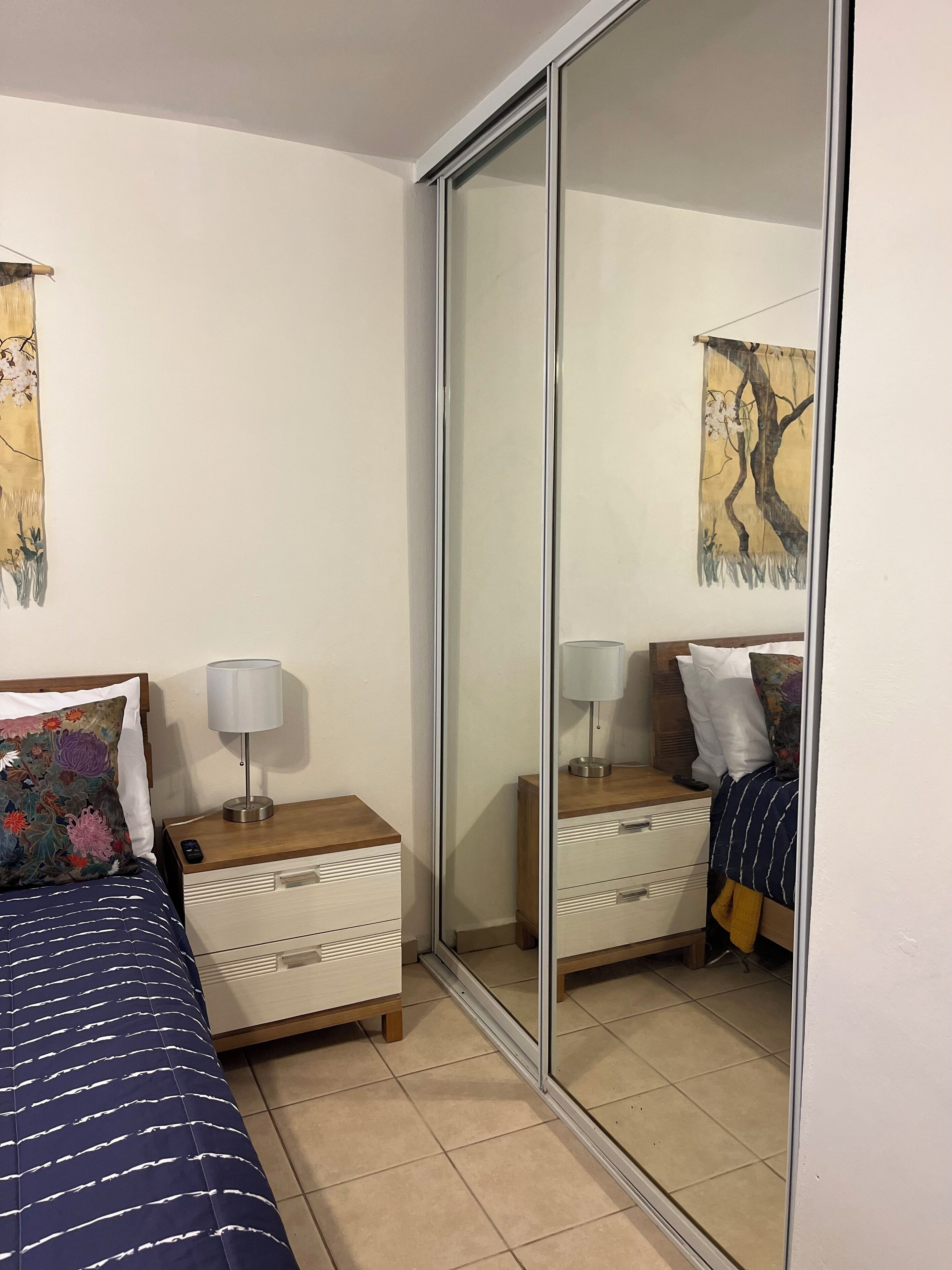 Ett hotellrum med en säng, två sängbord, en spegel och konstverk på väggarna.