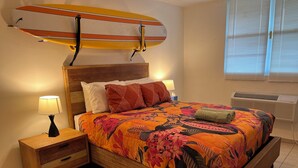 Une chambre à coucher avec un lit, des tables de chevet, une planche de surf et une fenêtre avec des stores.