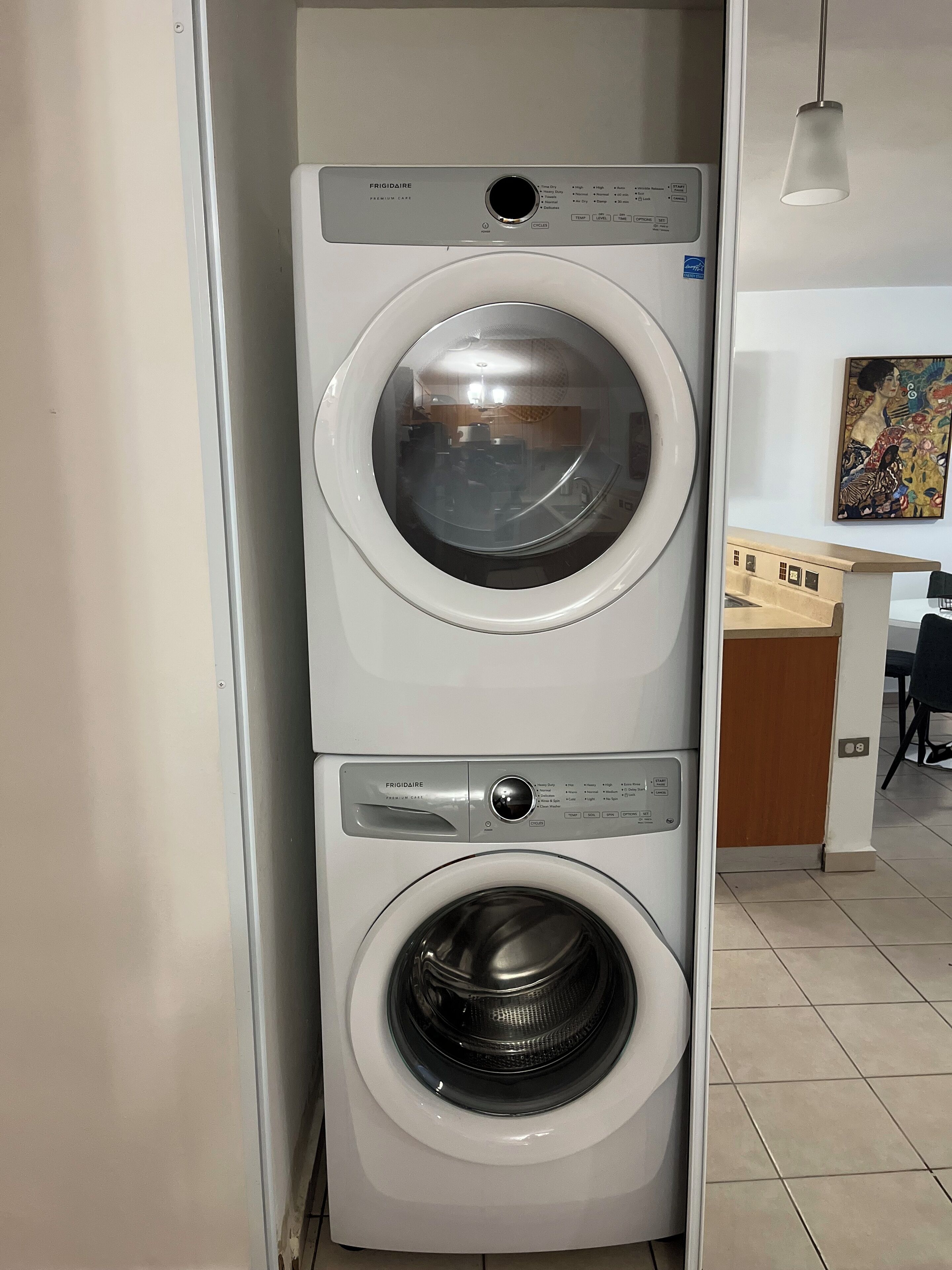 Eine Frontlader-Waschmaschine und ein Trockner von Frigidaire Premium Care in einem Hauswirtschaftsraum mit Fliesenboden und einem Bild an der Wand.