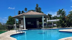 Une piscine d’un bleu éclatant, bordée de carreaux, un espace détente abrité et des palmiers en arrière-plan.