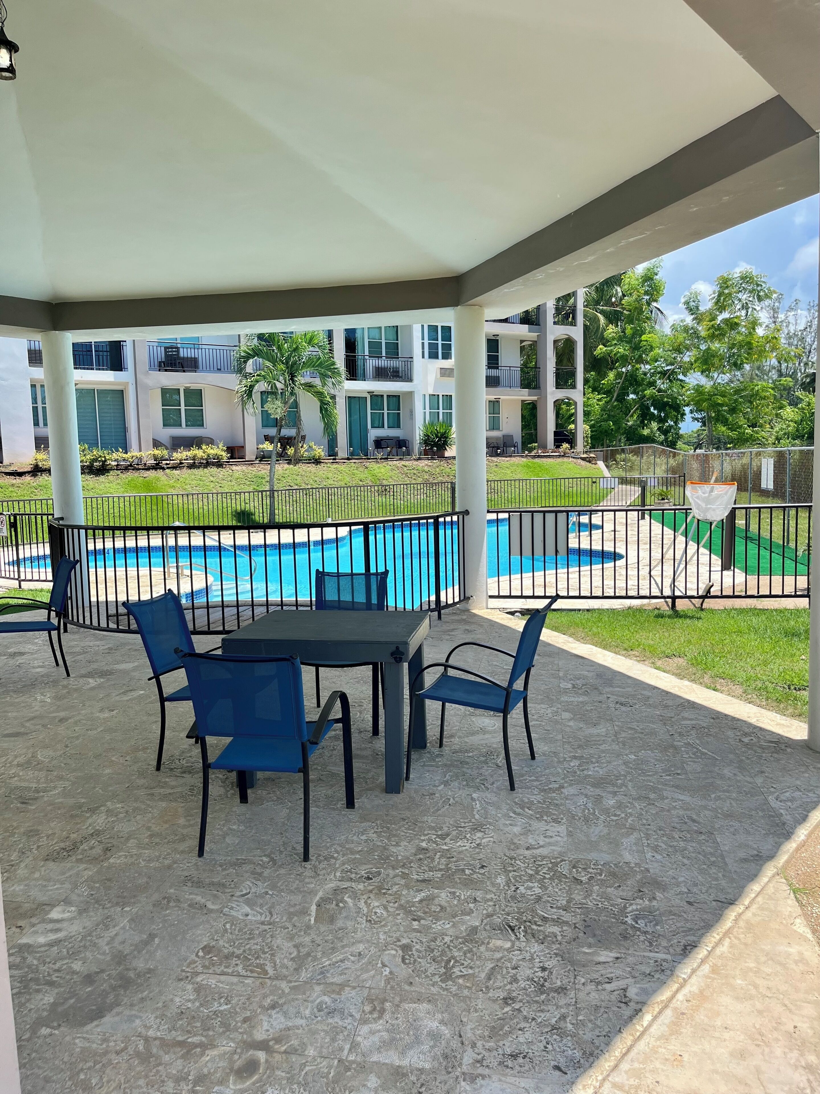 A covered outdoor area with a pool, blue chairs, and a table.