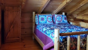 A wooden loft bedroom with a bed, wooden beams, and a sloped ceiling.