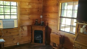 A wooden cabin interior with a fireplace, wooden furniture, and a television.