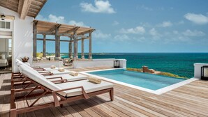 An infinity pool with lounge chairs, a wooden deck, and a view of the ocean. - 4 BR All-Inclusive Villa @ Ambergris Cay: Aurora (Big Ambergris Cay)