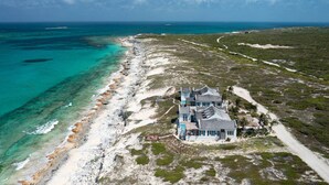 An aerial view of a large, single-story house with a spacious deck, located on a beach with clear turquoise waters and a sandy shoreline. - 4 BR All-Inclusive Villa @ Ambergris Cay: Aurora (Big Ambergris Cay)