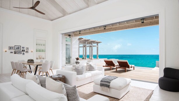 A spacious living room with a large window overlooking the ocean, furnished with white sofas and a dining area. - 4 BR All-Inclusive Villa @ Ambergris Cay: Aurora (Big Ambergris Cay)