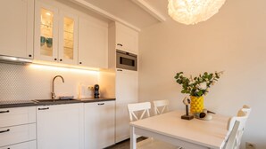 Une cuisine moderne avec des meubles blancs, un évier en acier inoxydable et un coin repas comprenant une table et des chaises blanches.