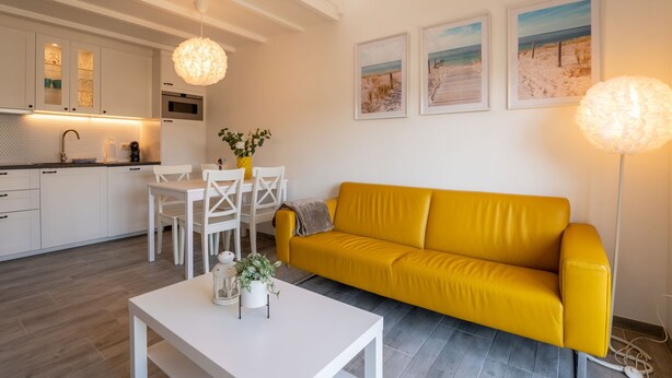Un salon moderne avec un canapé jaune, une table à manger blanche et une cuisine en arrière-plan.