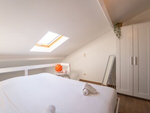 A bedroom with a skylight, a bed with rolled towels, a white wardrobe, and a small table with a decorative orange object.