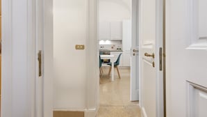 Un pasillo que conduce a una cocina con armarios blancos, una estufa y sillas color turquesa.