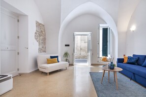Ein geräumiges Wohnzimmer mit einem weißen Sofa, einem blauen Sofa, einem runden Couchtisch und einem großen, rundbogigen Durchgang zu einem Außenbereich.